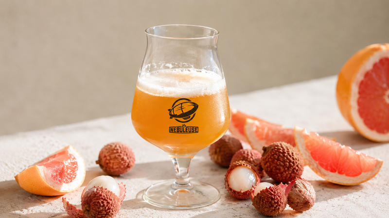 Un verre de bière avec du pamplemousse et des litchis à côté.